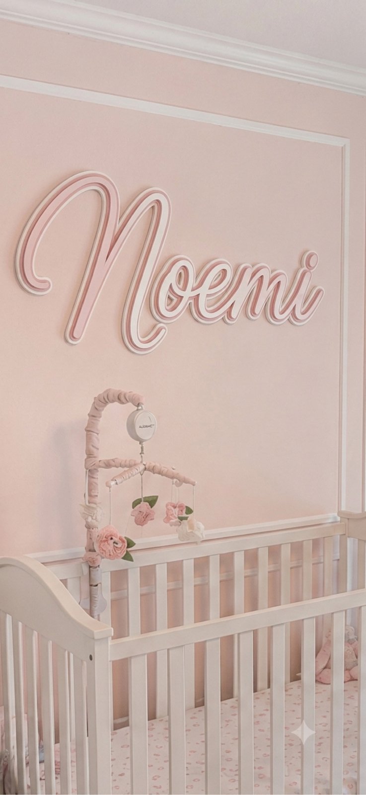 Script nursery name sign in blush pink above a crib - Noemi